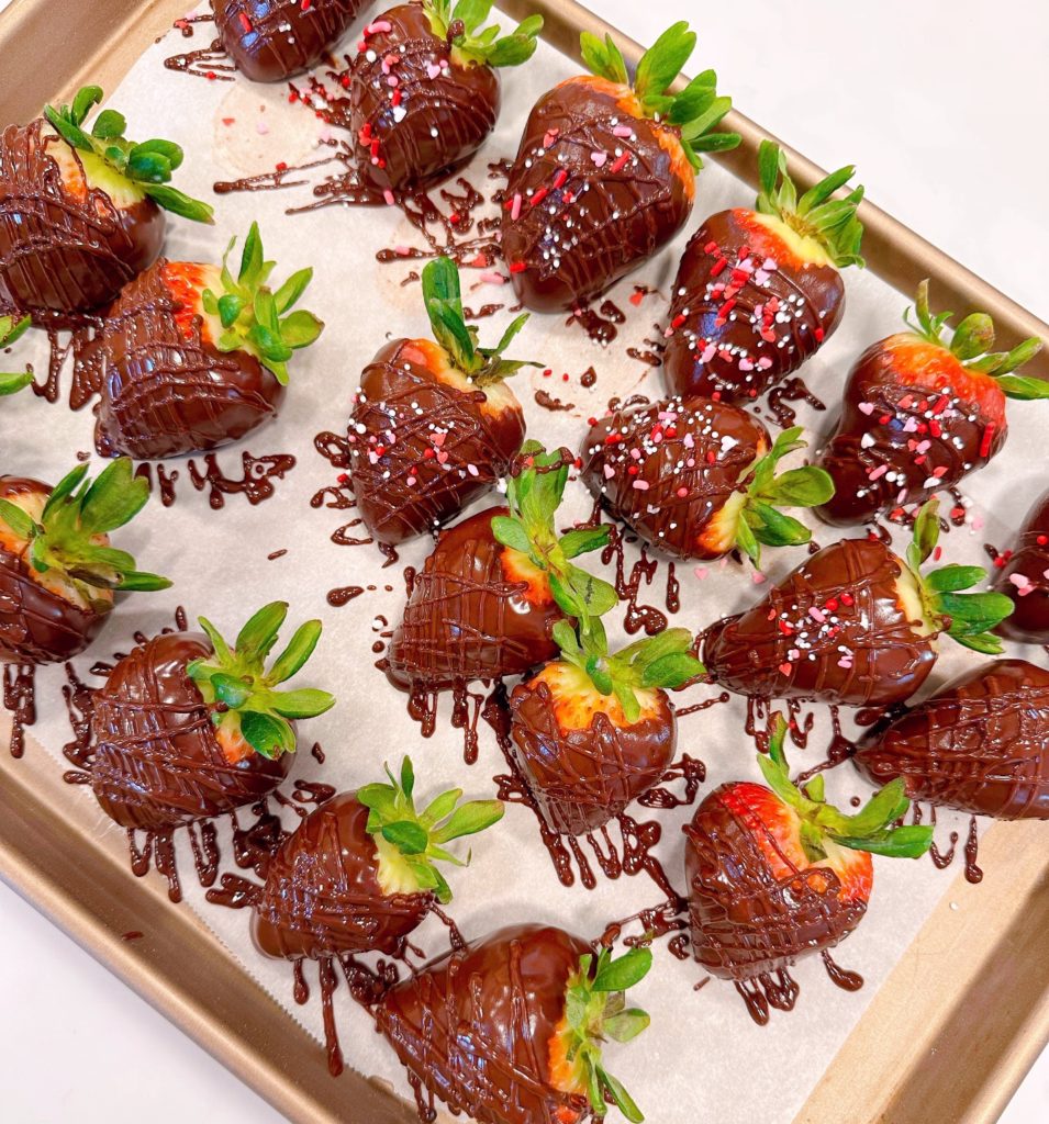 Berries drizzled with chocolate and sprinkles on a baking sheet.