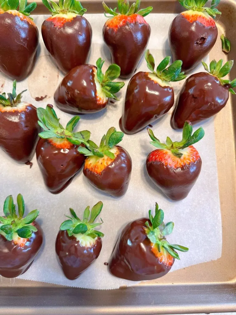 Strawberries dipped in chocolate on a parchment lined baking sheet.