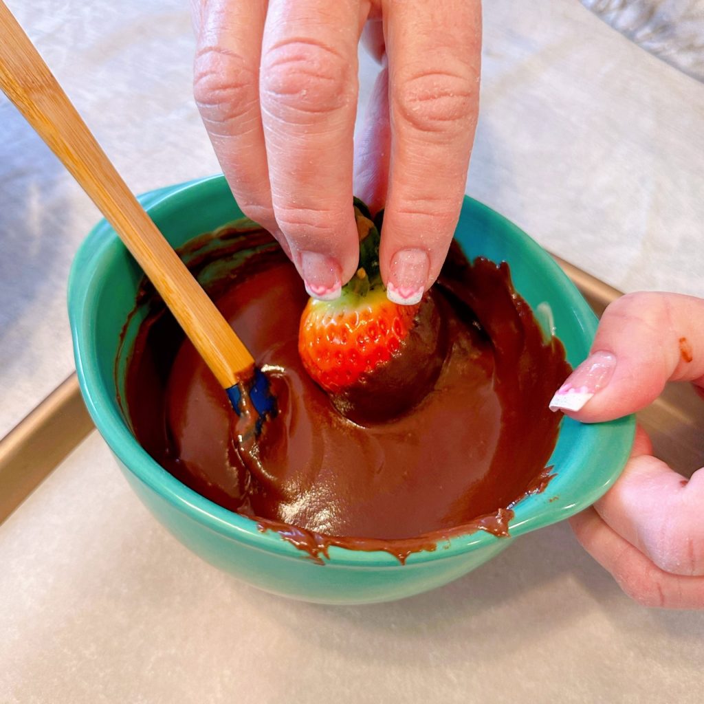 Dipping the strawberry into the melted chocolate.