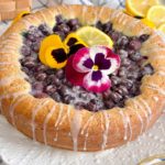 Blueberry Lemon Poppy seed cake with pansies and lemon glaze on a cake plate.