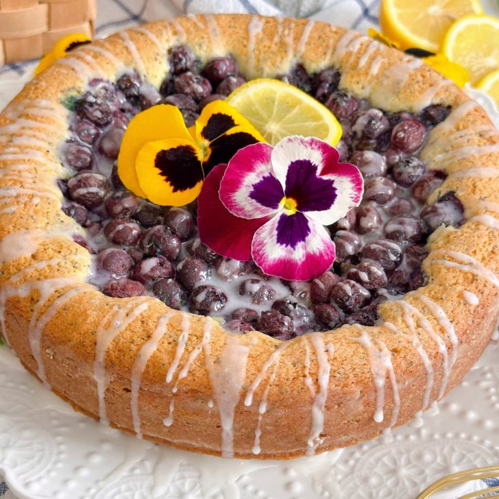 Blueberry Lemon Poppy seed cake with pansies and lemon glaze on a cake plate.