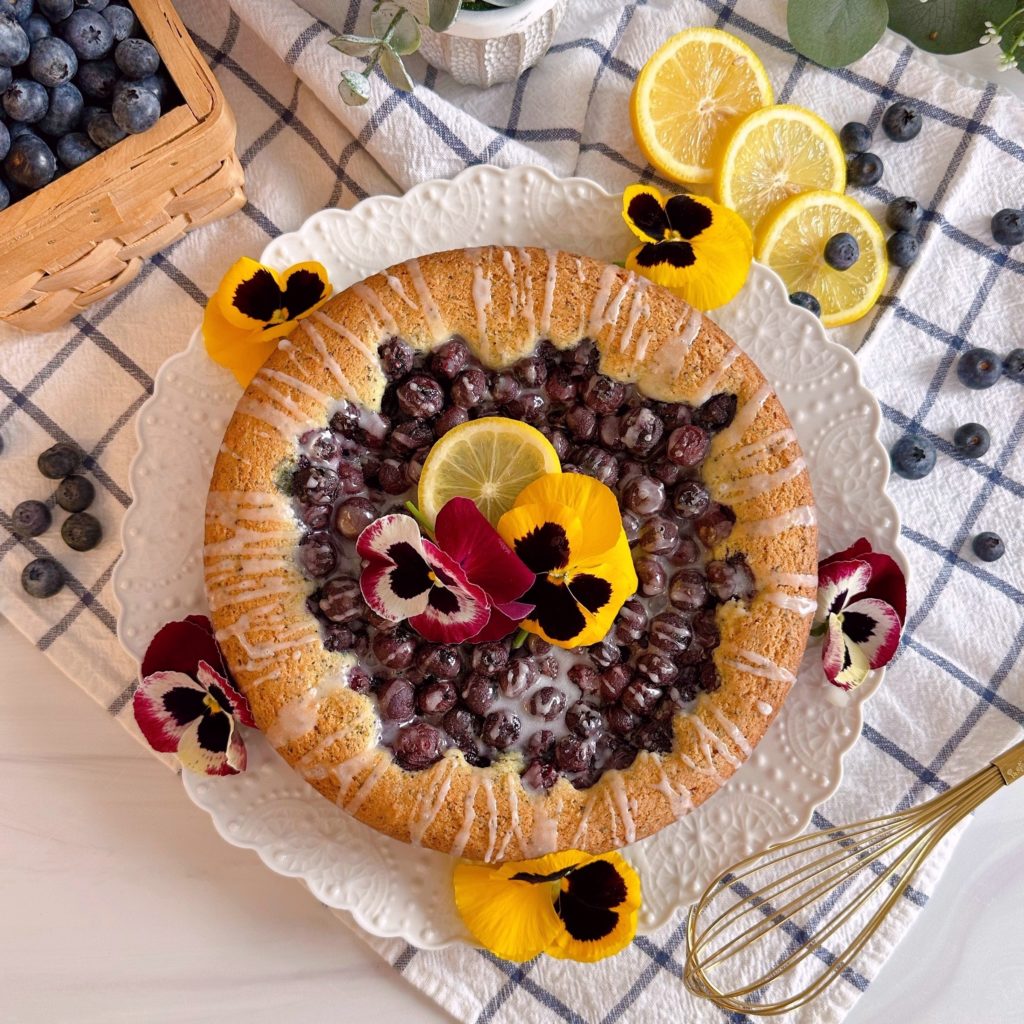 Blueberry-Lemon Poppy Seed Brunch Cake on a plate with flowers and lemon slices.